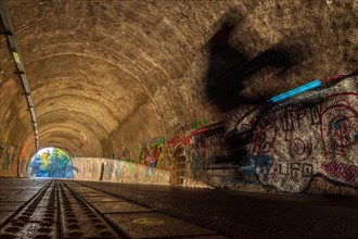 Blurred cyclist in a tunnel whose walls are covered with colourful graffiti, Nordbahntrasse,