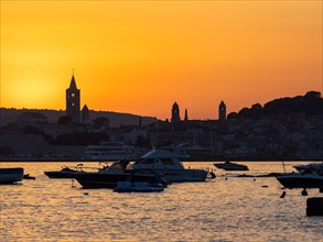 Boats anchoring in a bay, silhouette of church towers, evening mood after sunset over Rab, town of