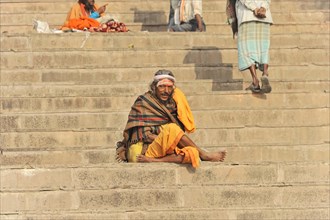 Relaxed looking man sitting on steps in front of an urban backdrop, Varanasi, Uttar Pradesh, India,