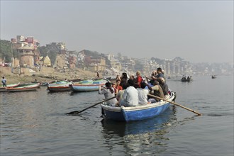 Boat with passengers on a river, rowers at the stern, city view in the light morning mist in the