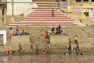 People on river steps, some bathing in the water, with a parasol in the background, Varanasi, Uttar