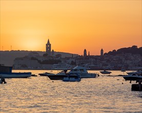 Boats anchoring in a bay, silhouette of church towers, evening mood after sunset over Rab, town of