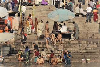 People bathing in the river on a sunny day with umbrellas on steps, Varanasi, Uttar Pradesh, India,