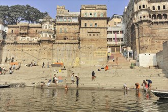 View of a busy stretch of river with urban ghats and historic buildings in the background,