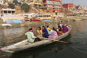 People on a boat on a river in front of a staircase with colourful buildings, Varanasi, Uttar