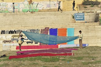 People hanging colourful laundry on a sunny riverside staircase, Varanasi, Uttar Pradesh, India,
