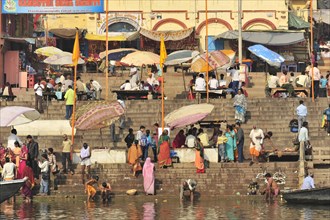 Lively social scene with many people and parasols at the ghats of a river, Varanasi, Uttar Pradesh,