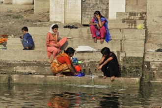 Three woman in traditional dress sitting at the ghats and chatting, Varanasi, Uttar Pradesh, India,