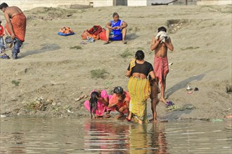A family performs a traditional ritual at the water's edge of a beach, Varanasi, Uttar Pradesh,