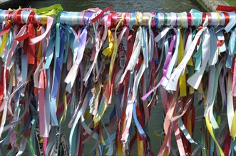 Vibrant colorful ribbons tied to a bridge's railing over water, representing a festive or cultural