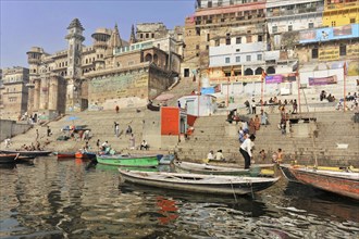 Busy riverbank with boats and people against the backdrop of urban architecture, Varanasi, Uttar
