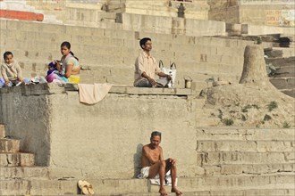 Several people sit relaxed on the ghats of a river and interact with each other, Varanasi, Uttar