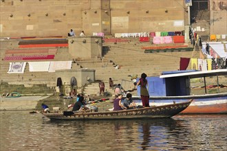 Travellers on a small boat enjoying the river scenery near a clothesline, Varanasi, Uttar Pradesh,