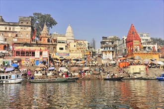 A busy ghat with people, boats and temples on the riverbank, Varanasi, Uttar Pradesh, India, Asia