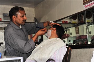 Hairdresser giving a customer a traditional shave in a hairdressing salon, Varanasi, Uttar Pradesh,