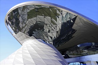 A modern building with a reflective glass facade under a clear blue sky, BMW WELT, Munich, Germany,