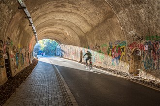 A person on a bicycle rides through a tunnel decorated with graffiti, Nordbahntrasse, Elberfeld,