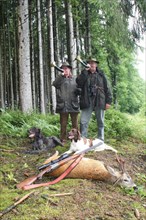 Huntsman and huntress blowing their hunting horns at a shot roebuck according to old tradition,