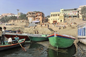 People and boats on the lively riverbank with visible city steps, Varanasi, Uttar Pradesh, India,