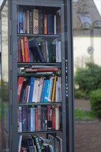 Open bookcase, close-up, many colourful books in a glass case, outdoor, in the background blurred