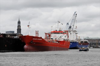 Red tanker in harbour water under cloudy sky, surrounded by harbour facilities, Hamburg, Hanseatic