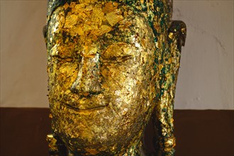 Close-up of a Buddha head adorned with gold leaf, showing texture and age