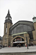 Historic railway station with tower clock and people walking past the entrance, Hamburg, Hanseatic