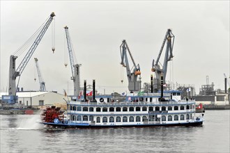 A classic paddle steamer sails past harbour cranes, accompanied by a slightly cloudy sky, Hamburg,