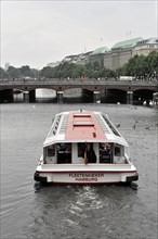 An excursion boat on an urban river under a bridge on a cloudy day, Hamburg, Hanseatic City of