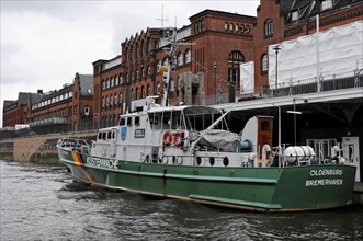 Coastguard boat at the pier near old brick building under cloudy sky, Hamburg, Hanseatic City of