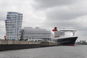 A Queen Mary 2 cruise ship moored in the harbour next to modern waterfront buildings, Hamburg,