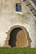 Entrance gate, window and part of the wings of the windmill Auf der Hoechte under a cloudless blue