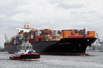A large container ship loaded with colourful containers escorted by a tugboat, Hamburg, Hanseatic