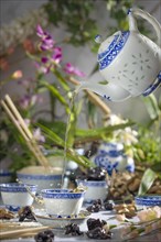 Tea splashes out of the bowl of an Asian tea set as it is poured, flying pot, flowers in the
