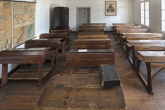 Classroom with school desks and teacher's desk from the 19th century, behind a photograph of Tsar