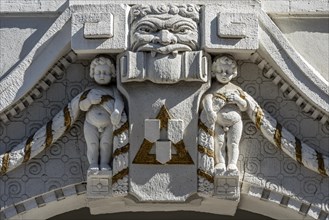 Decorative figures above gateway in Art Nouveau style, naked boys with garland, grim male face,