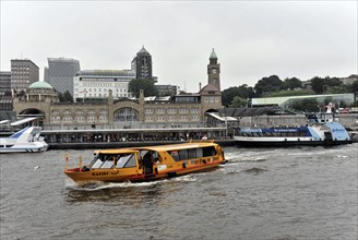 A yellow harbour ferry with passengers sailing on the water against an urban background, Hamburg,