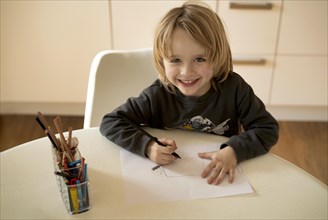 Indoor photo, boy, 4-5 years, blond, painting on sheet of paper, pencils, table, laughing,