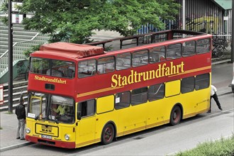 A yellow and red double-decker sightseeing bus at a bus stop with a person nearby, Hamburg,