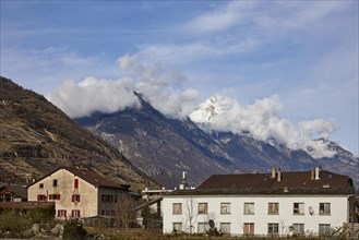 Residential buildings and pointed, high mountains with clouds in Martigny, district of Martigny,
