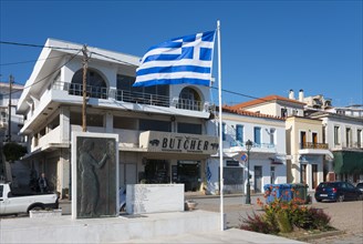 Greek flag in front of a building with the inscription 'BUTCHER' and a statue sculpture, Galatas,