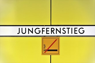 Sign of the underground station 'Jungfernstieg' with no smoking sign on yellow background, Hamburg,