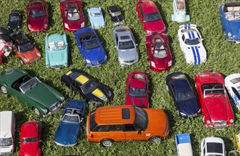 Model cars that look confusingly similar to the originals stand in a meadow at a flea market stall,