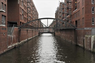A pedestrian bridge over a water channel with brick buildings on the sides, Hamburg, Hanseatic City