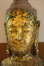 Weathered Buddha head covered with gold flakes, displaying a serene expression