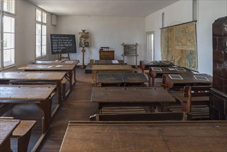 School desks, chalkboard and map, on the right a tiled stove in a classroom from the 19th century,