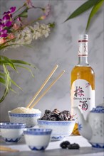 Asian tea set with blue patterns, a bottle of Chinese plum wine, dried fruit and a bowl of rice