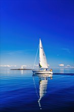 German sailboat sailing in an archipelago with water reflection in the sea and a lighthouse on a