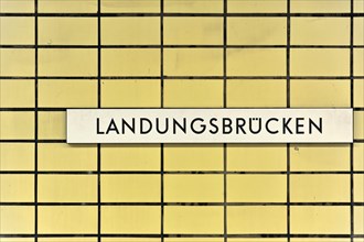 A sign with the inscription 'Landungsbruecken' on a yellow tiled wall, Hamburg, Hanseatic City of
