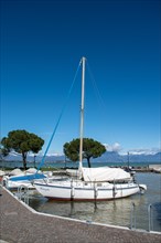 A sailing boat moored in the harbour with clear blue sky and mountain in the background, Sirmione,